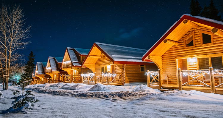 A row of wooden cabins covered in snow and lit up at night